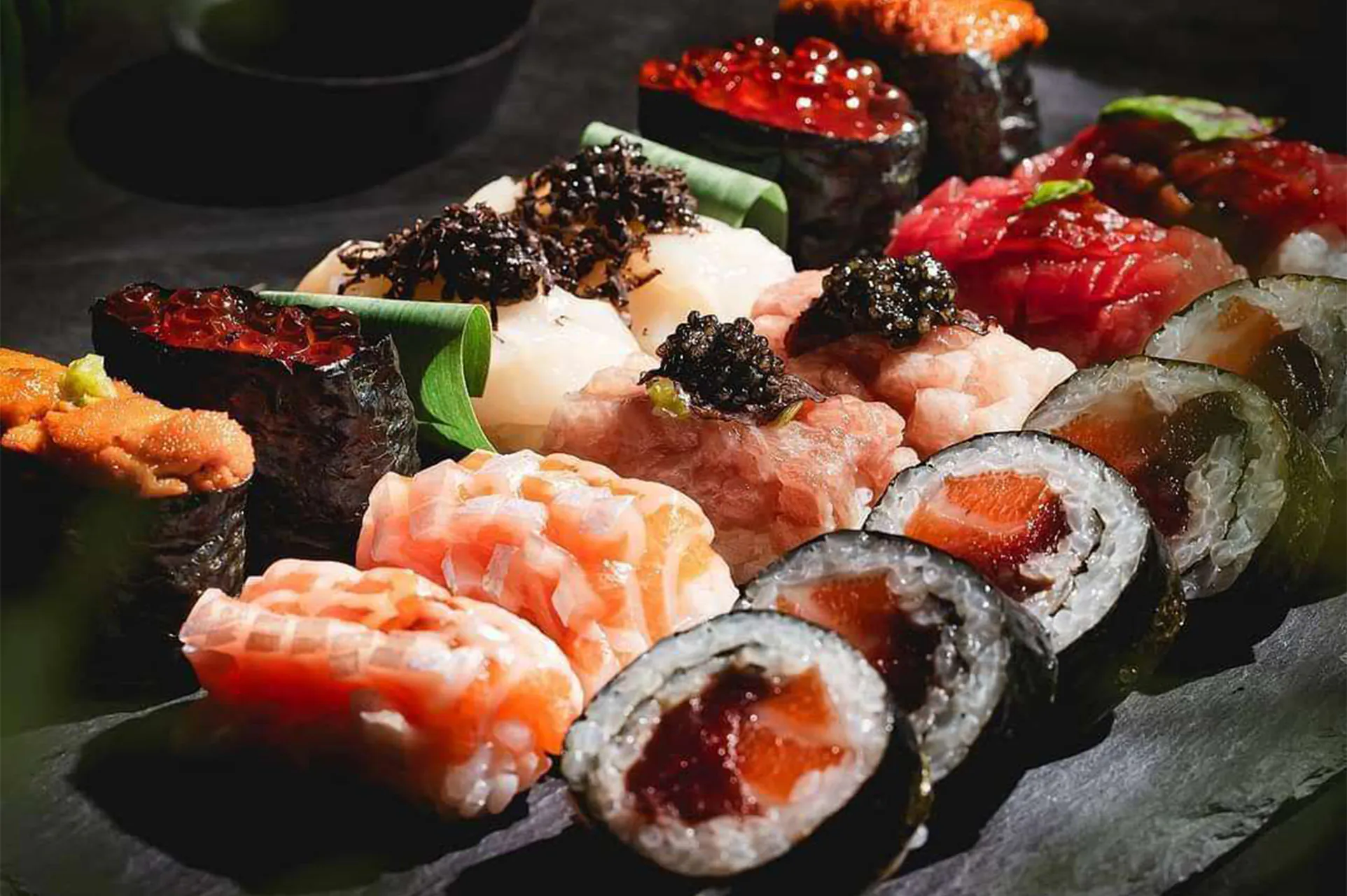 Assorted sushi platter with nigiri, rolls, and caviar on slate.